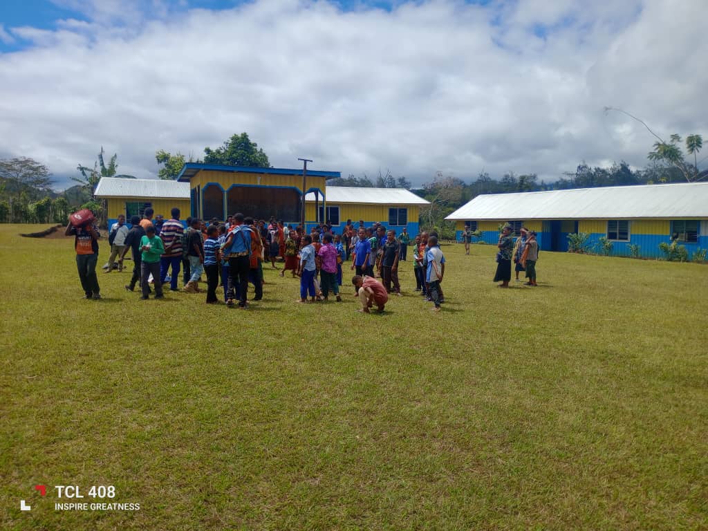 Students, teachers, and community members gathered outside the yellow and blue school buildings at Akaka Community School.