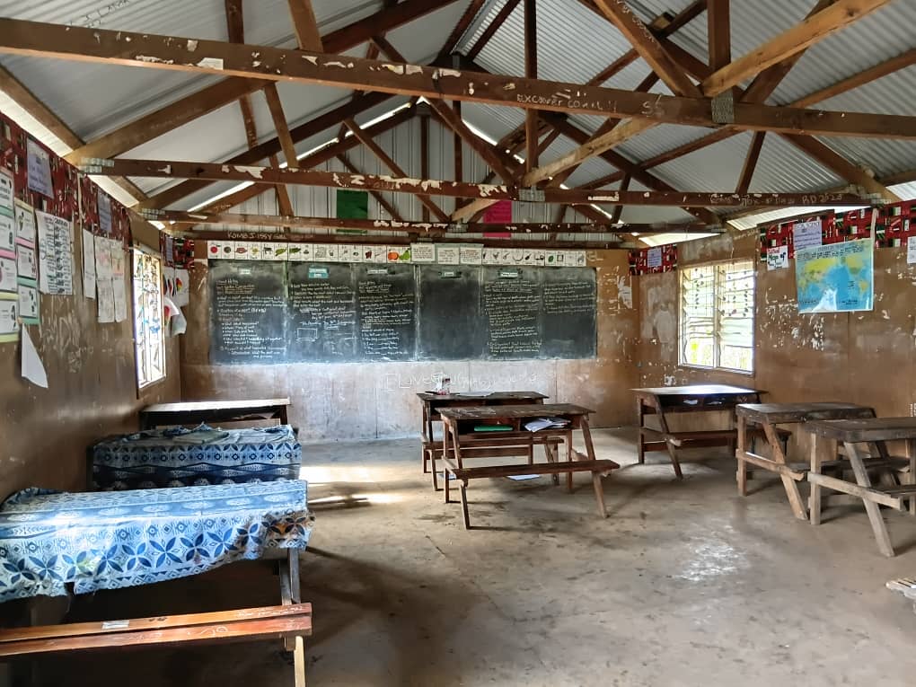 Interior of a classroom at Akaka Community School showing wooden desks, blackboards, and a world map on the wall.