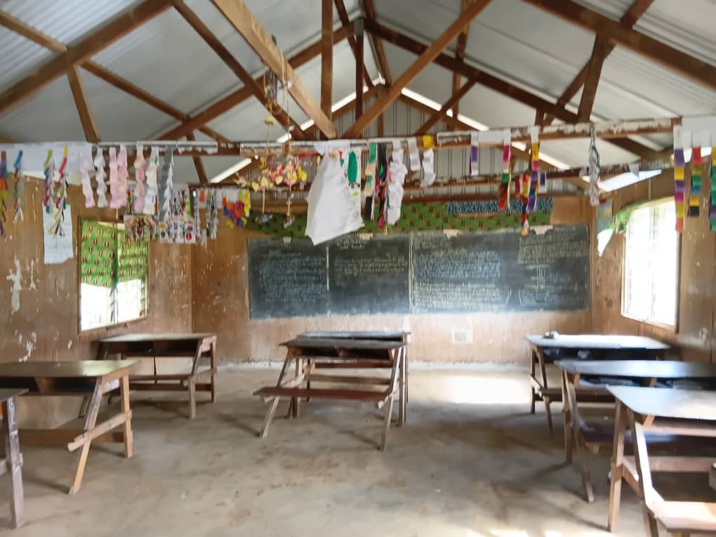 Interior of a classroom at Akaka Community School showing wooden desks, a large blackboard, and student artwork hanging across the room.