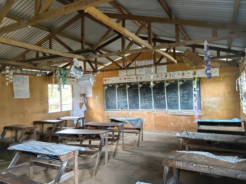 Interior of a classroom at Akaka Community School with wooden desks, blackboards, and educational posters on the walls.