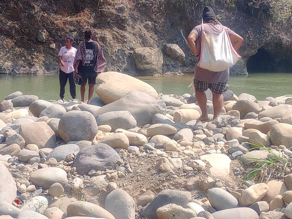 People standing on smooth river rocks at the edge of a low river in Kun Valley