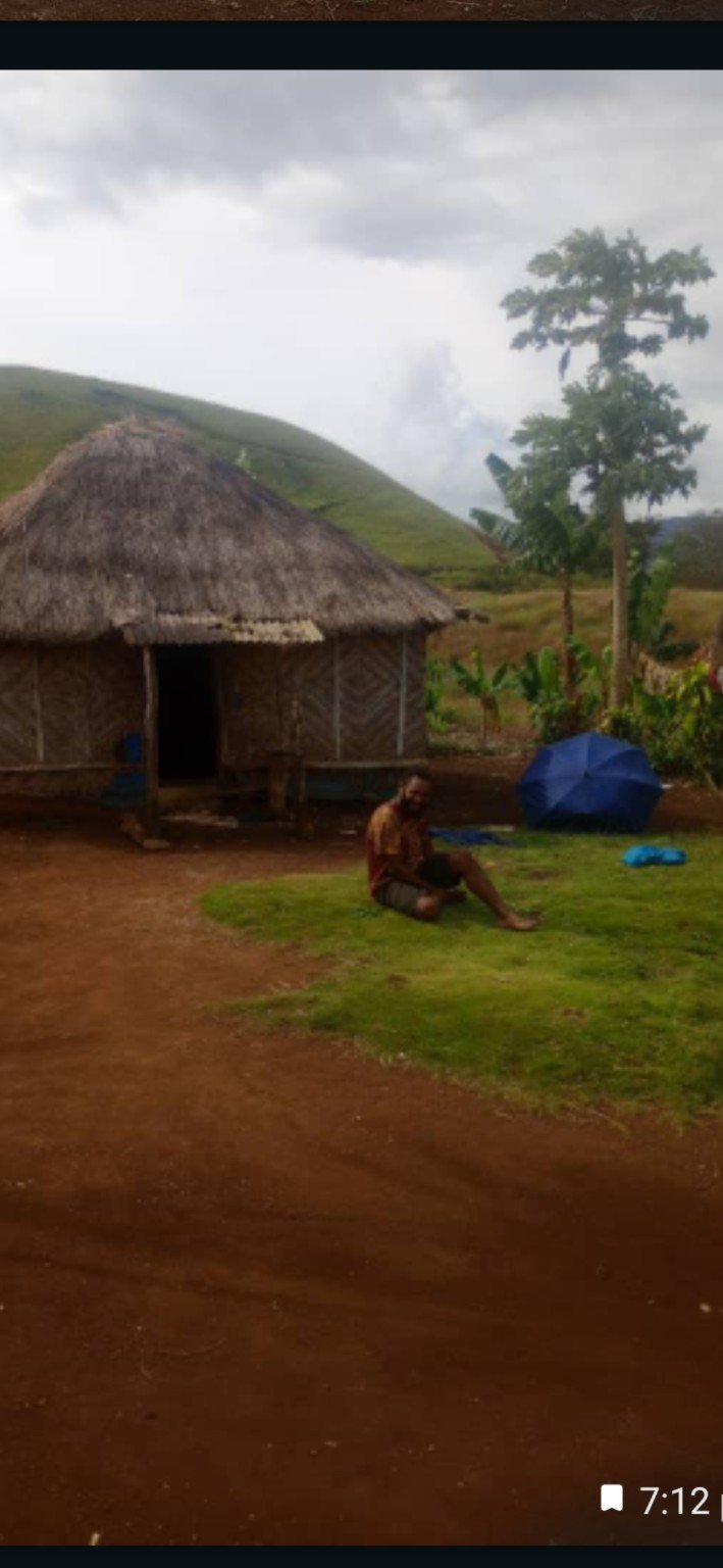 A man sitting outside a round thatched hut in the highlands